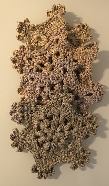 Vertikale Girlande aus gehäkelten, beigefarbenen Schneeflockenmotiven mit sichtbarer Struktur