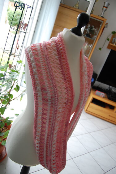 Gehäkelter Loop-Schal in Rosa und Weiß mit offenem Muster auf einer Schaufensterpuppe.