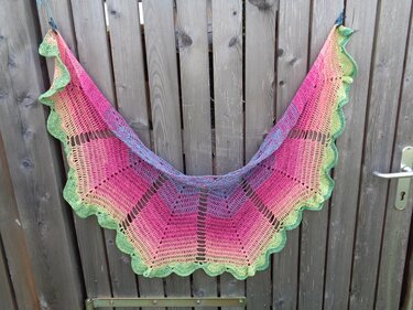 Halbrundes Häkeltuch in Pink, Orange und Grün mit Rüschenrand an Holzzaun