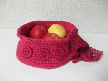 Small pink crochet storage basket with three floral appliqués and lace edge holding apples