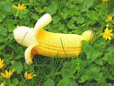 Nahaufnahme eines gehäkelten Bananen-Schmusetiers mit halb geöffneter Schale im Gras