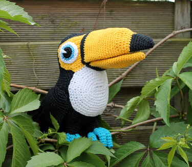 Nahaufnahme gehäkelter Tukan mit gelbem Schnabel und blau-türkisen Füßen