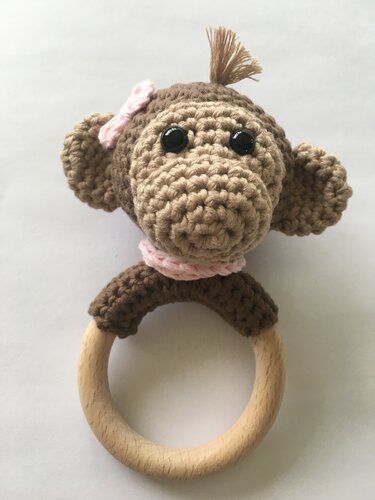 Gehäkelter braun-beiger Affenkopf mit rosa Schleife auf rundem Holzring.