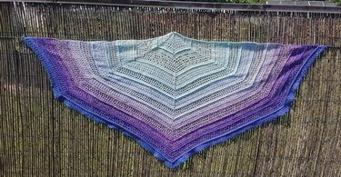 Gehäkeltes Dreieckstuch in Mint-, Blau- und Violetttönen mit offenem Muster, aufgehängt an einem Sichtschutz