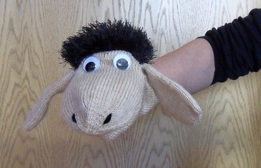 Beige gestrickte Schaf-Handpuppe mit schwarzem Haar und großen Wackelaugen