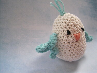 Kleines gehäkeltes Vogel-Amigurumi in Creme mit türkisfarbenen Flügeln, Aufhängeschlaufe und orangefarbenem Schnabel