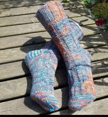 Handgestrickte mehrfarbige Socken mit Rippbündchen auf Holzplanken.