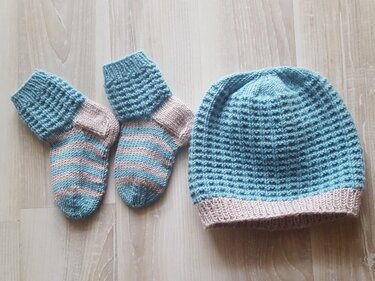 Gestrickte hellblaue Babymütze mit zartrosa Bündchen neben zwei passenden gestreiften Babysöckchen