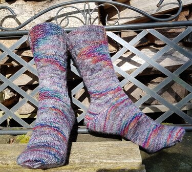Gestrickte Socken, grau-meliert mit bunten Farbakzenten, auf Metallgitter vor Holzstapel