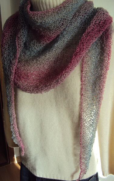 Handgestricktes Dreieckstuch mit offenem Muster und Farbverlauf von Pink zu Hellblau auf hellem Hintergrund