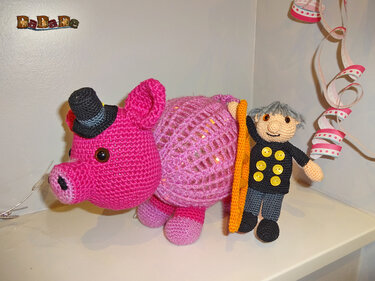 Gehäkeltes pinkes Glücksschwein mit schwarzem Zylinder und Amigurumi-Schornsteinfeger mit Leiter vor Partydekoration.
