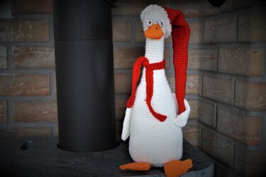 Gehäkelte weiße Gans mit langer roter Zipfelmütze und rotem Schal vor Ziegelwand