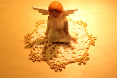 Engel auf weißem Häkeldeckchen mit goldener Bordüre, warm beleuchtet