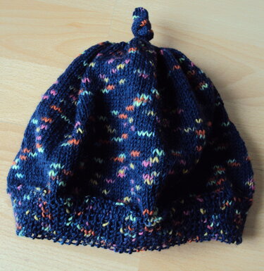 Dunkelblaue gestrickte Mütze mit bunten Sprenkeln und gedrehtem Knoten