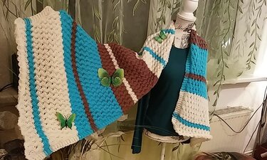 Breiter gestrickter Schal in Creme, Türkis und Braun mit offenem Strukturmuster auf einer Schneiderpuppe, verziert mit grünen Schmetterlingsdekorationen
