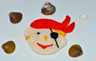 Bunt gehäkelter Piratenkopf mit rotem Kopftuch und schwarzer Augenklappe, dekorativ präsentiert