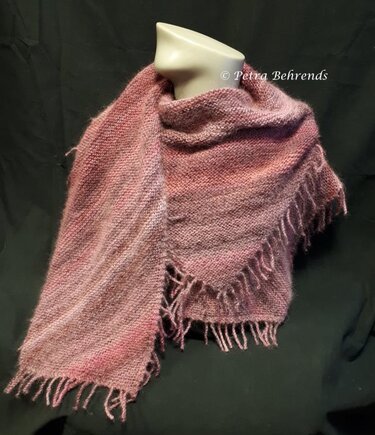 Gestrickter Dreiecksschal in Rosétönen mit Fransen, drapiert auf einer Schaufensterbüste vor dunklem Hintergrund