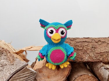 Bunte gehäkelte Amigurumi-Eule auf Holzstapel