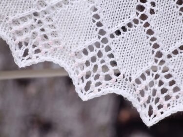 Nahaufnahme weißer Strickkante mit Lochmuster und zartrosa Perlen