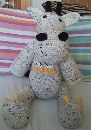 Gehäkelter grau-melierter Amigurumi-Dino mit schwarzen Hörnern, Knopfaugen, gelben Krallen und gelbem Zierkragen