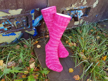 Handgestrickte wadenhohe Herrensocken in kräftigem Rosa auf Holz vor verwitterter Metalltür