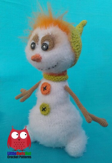 Fuzzy crocheted amigurumi snowman with spiky orange hair, pointed green hat, striped scarf, button accents and crocheted arms on a blue background.