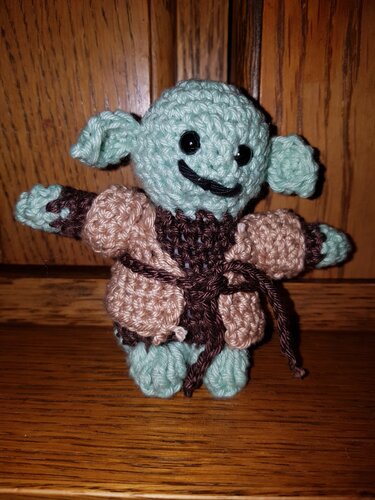 Gehäkelte Mini-Amigurumi mit mintgrünem Kopf, großen Ohren und brauner Robe vor Holz