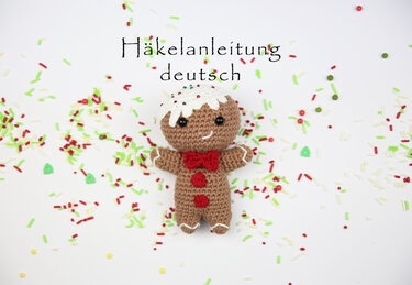 Gehäkelter Lebkuchenmann Amigurumi mit weißem Zuckerguss, roter Schleife und bunten Streuseln, Text 'Häkelanleitung deutsch'