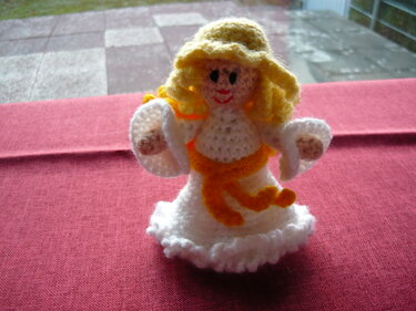 Gehäkelter Amigurumi-Engel mit weißem Kleid und gelbem Gürtel auf rotem Stoff