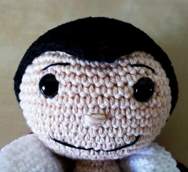 Gehäkelter Amigurumi-Puppenkopf mit glänzenden schwarzen Augen, gesticktem Lächeln und dunklem Haar.