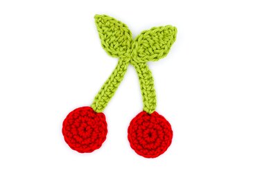 Gehäkelte rote Kirschen mit grünen Stielen und Blättern auf weißem Hintergrund