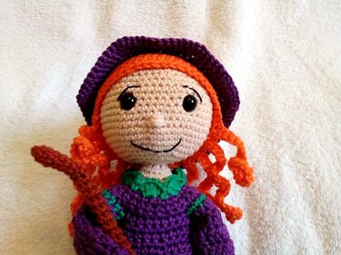 Gehäkelte Amigurumi-Puppe mit orangefarbenen Locken, lila Hut und kleinem Besen