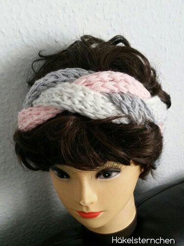 Gehäkeltes Stirnband mit Zopfmuster in Rosa, Weiß und Grau auf einer Schaufensterpuppe.