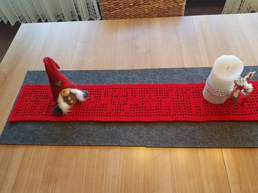 Roter gehäkelter Tischläufer mit Sternenmuster, dekoriert mit Weihnachtsfiguren auf einer Holztischplatte.
