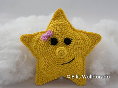 Gepolstertes gelbes Stern-Amigurumi mit rosa Schleife und lächelndem Gesicht auf weichem Hintergrund