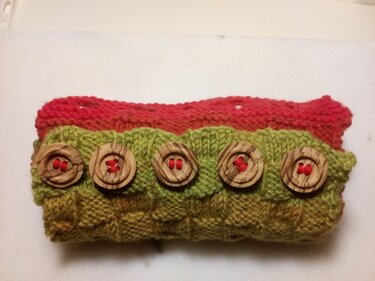Schmaler gestrickter Loop in Grün und Rot mit fünf Holzknöpfen und roten Garnstichen