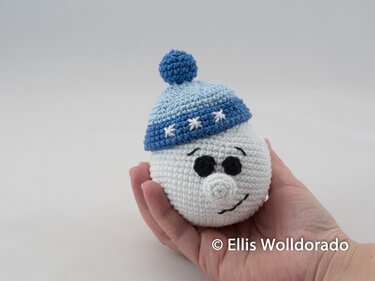 Gehäkelter Schneemannkopf mit blauer Mütze in einer Hand