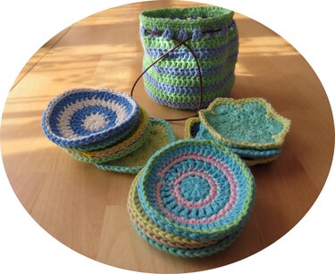 Gestapelte runde und blütenförmige gehäkelte Untersetzer neben einem gestreiften Aufbewahrungskorb mit Kordel auf Holztisch