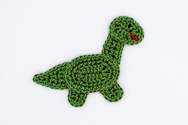 Grüne gehäkelte Dino-Applikation mit rotem Mund auf weißem Hintergrund