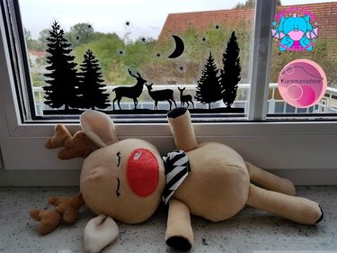 Plüsch‑Rentier vor Fenster mit schwarzer Wald‑ und Hirschsilhouette