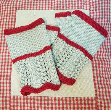 Zwei hellgraue gestrickte fingerlose Handschuhe mit rotem Rand und Lochmuster.