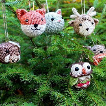 Mehrere gehäkelte Tiergesichter als Kugel-Anhänger in Tannenzweigen, darunter Fuchs, Katze, Rentier und Eule