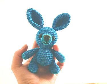 Hand hält Mini-Amigurumi-Hase aus türkisfarbenem Garn; sichtbare Maschen und Ohren