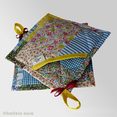 Zwei gepatchworkte Topflappen mit Blumen-, Streifen- und Vichy-Karo-Mustern sowie gelben Aufhängeschlaufen