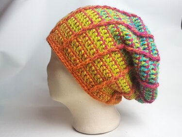 Mannequinkopf mit gehäkelter, mehrfarbiger Slouch‑Mütze in Orange, Gelb, Pink und Türkis