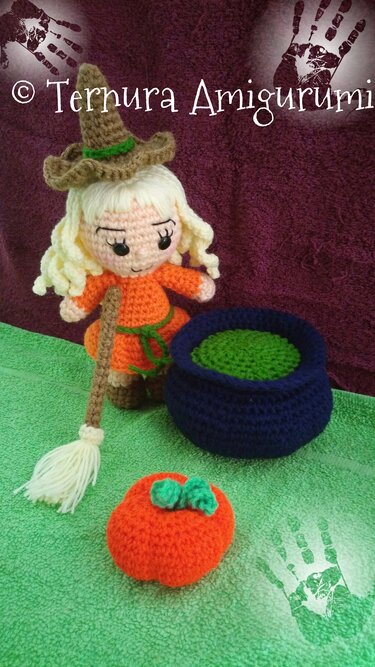 Hand-crocheted amigurumi witch in orange dress with broom, blue cauldron and orange pumpkin