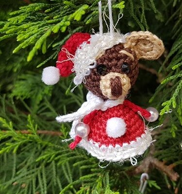 Gehäkeltes kleines Bärchen im roten Weihnachtskleid mit Mütze und Schal als Christbaumanhänger im Tannengrün.
