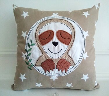 Beiges Sternenkissen mit appliziertem Faultier, braunen Augenpartien und grüner Blattstickerei