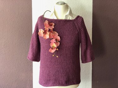 Dunkellila gestrickter Damenpullover mit Dreiviertelärmeln und U-Boot-Ausschnitt auf Schaufensterpuppe, dekoriert mit rosa Orchideen