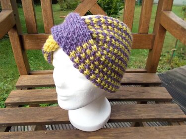 Schaufensterkopf mit gestricktem Stirnband in Lila und Gelb mit gedrehter Vorderseite auf Holzbänkchen